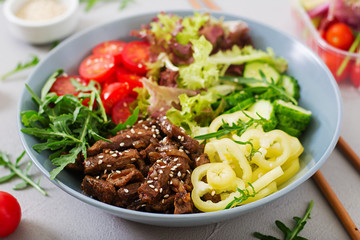 Salad with beef teriyaki and fresh vegetables - tomatoes, cucumbers, paprika, arugula and lettuce in bowl.