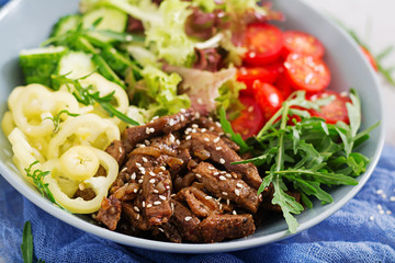 Salad with beef teriyaki and fresh vegetables - tomatoes, cucumbers, paprika, arugula and lettuce in bowl.