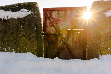 sun shining through rustic red metal gate and rock wall in winter in the Swiss alps
