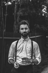 Young man with a beard and cigar dressed fashionable in modern clothes with suspenders.