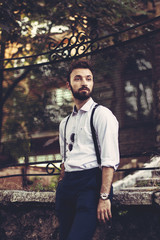Fototapeta na wymiar Young man with a beard and cigar dressed fashionable in modern clothes with suspenders.