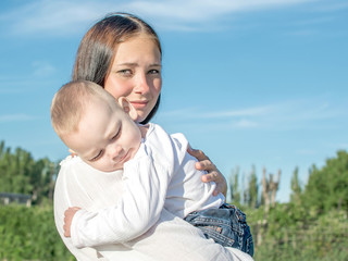 Young beautiful mother and baby boy hugging on nature in summer. Pretty woman Holding sleeping child in her arms