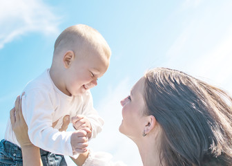 Young beautiful mother Tossing up baby boy on blue sky background in summer sunny day