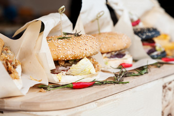 Many hamburgers wrapped in paper on a wooden table, side shot, selective focus