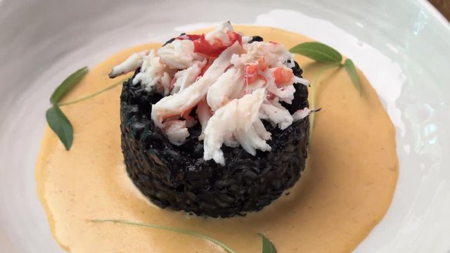 black rice with crab meat on a white plate in the sauce