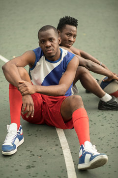 Two african american man friends sitting on street basketball court