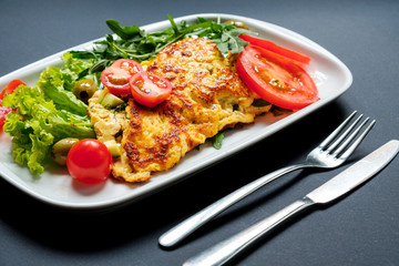 Salad of fried tofu with tomatoes and rocula. Homemade vegetarian salad in a white plate on a black background. A healthy Asian diet vegan vegetarian salad.