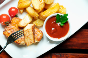 Vegetarian dinner. Fried tofu with spices, potatoes with fresh tomatoes. On a white plate, wooden background.