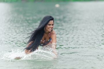 Young beautiful black-haired woman posing on the beach in the water