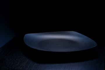 View of black empty plate on dark grey background. Black background black plate view. Square plate