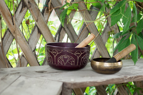 wo Tibetan singing bowls with sticks on a wooden bench in a garden