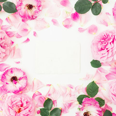 Pink rose flowers, leaves, petals and white envelope on white background. Flat lay, top view