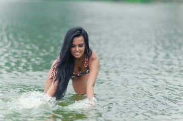 Young beautiful black-haired woman posing on the beach in the water