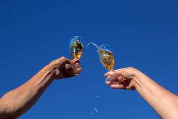 Hands of man and woman clink wineglasses of sparkling white wine on blue sky