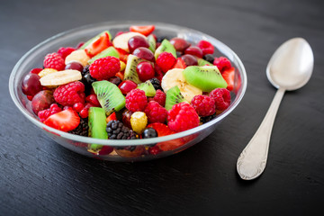Fruit salad in glass plate on dark background. Natural breakfast
