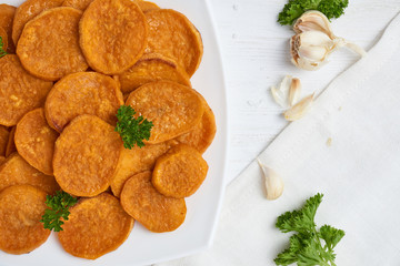 Baked sweet potatoes in white plate on a white wooden table with parsley, garlic and salt. White wooden rustic picnic table scenery from above.