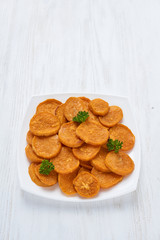Baked sweet potatoes in white plate on a white wooden table with parsley, garlic and salt. White wooden rustic picnic table scenery from above.