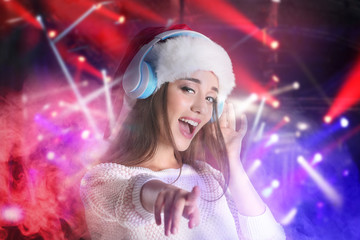 Young woman with headphones listening to music on blurred lights background. Christmas and New Year...