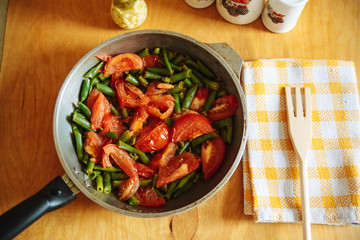 Tomatoes with cheese and green beans in a frying pan.