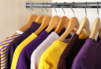 Wooden hangers with clothes in wardrobe. Combination of lilac and yellow colors