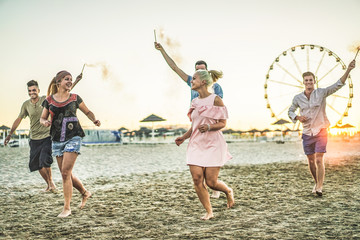 Group of happy friends running on the beach with fireworks sparklers - Young people having fun in...