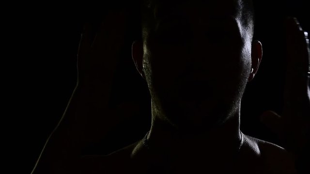 Man in the dark emotionally sings. Silhouettes of men, portrait in dark studio, shadows and lighting, head and hands. The singer sings song with emotion. Music video of unrecognizable young guy