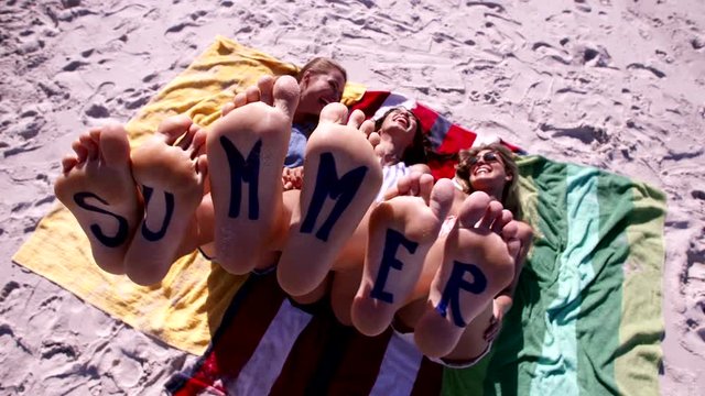 Bare feet of female friends with word summer. Video of three young women lying at the beach enjoying summer vacation.