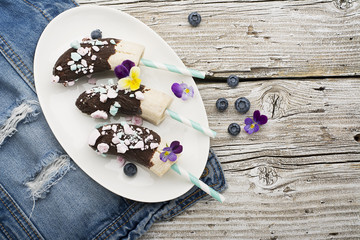 Chocobanana Light summer refreshing dessert made from frozen banana Eskimo in a glaze made of dark chocolate and colored meringue on a cocktail tube on a light background. Top View