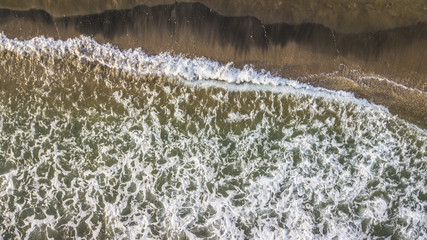 Vista aerea perpendicolare delle onde del mar Tirreno che si infrangono sulla costa. L' impatto con il bagnasciuga crea la schiuma bianca. La spiaggia d'inverno è vuota.