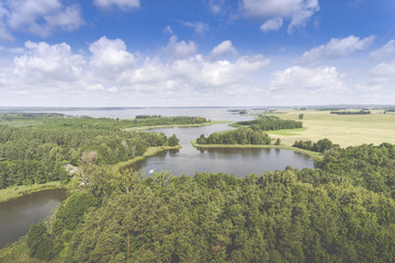 Aerial view of green islands and clouds at summer sunny morning. Masurian Lake District  in Poland. Wonders of the world from above. Yachts sailing in the lake.