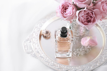 Metal tray with bottle of perfume and flowers on light background