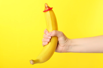 Woman holding banana with condom against color background. Safe sex concept