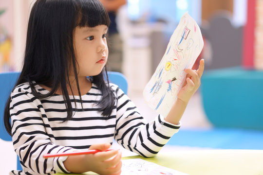 Asian children cute or kid girl learning for coloring or drawing paint on white paper and colorful table with chair at nursery or pre school on soft focus