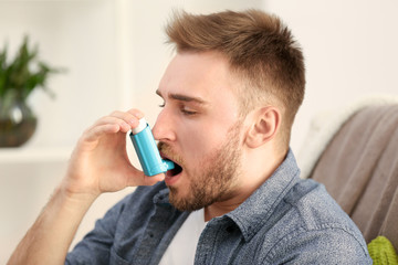 Young man using inhaler for asthma and respiratory diseases at home - obrazy, fototapety, plakaty