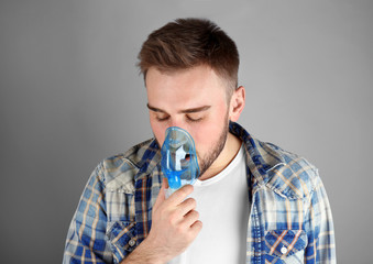 Young man using nebulizer for asthma and respiratory diseases on light background