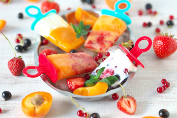 Homemade popsicles with berries, yogurt, mint,apricots,peaches, and strawberries on a rustic plate with ice
