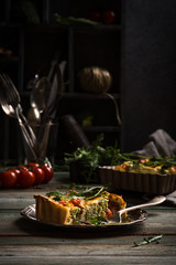 Slice of delicious homemade quiche with cherry tomatoes and broccoli on metal plate. Dark photo of healthy vegetarian food.