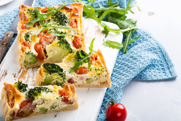 Delicious vegetarian homemade pie, sliced quiche with cherry tomatoes, broccoli and herbal cheese on old white cutting board. Healthy food concept.