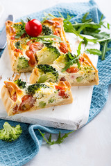 Delicious vegetarian homemade pie, sliced quiche with cherry tomatoes, broccoli and herbal cheese on old white cutting board. Healthy food concept.