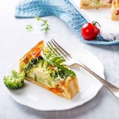 Slice of delicious vegetarian homemade quiche with cherry tomatoes and broccoli on white plate. Healthy food concept.