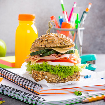 Healthy lunch for school with sandwich, fresh apple and orange juice. Assorted colorful school supplies.