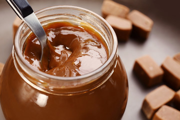 Glass jar with tasty caramel sauce and spoon on table
