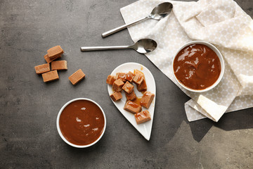 Bowls with tasty caramel sauce and candies on table