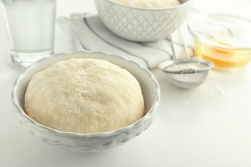 Bowl with raw dough and ingredients on white table
