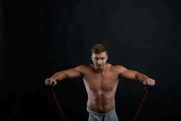 Fototapeta na wymiar People, sports, fitness, health and active lifestyle concept. Picture of confident determined young athlete strenghtening arms using a rubber band, looking at camera with concentrated expression