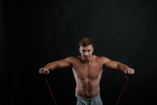 People, sports, fitness, health and active lifestyle concept. Picture of confident determined young athlete strenghtening arms using a rubber band, looking at camera with concentrated expression