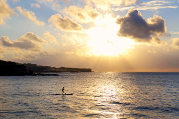 A silhouette of man doing paddle boarding in the golden morning light