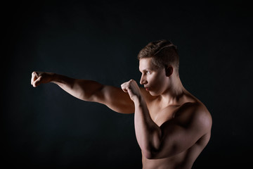 Fototapeta na wymiar Profile portrait of strong young European sportsman with naked muscular torso boxing, punching air in front of him. Attractive shirtless male boxer or kickboxer exercising in gym. Martial arts concept