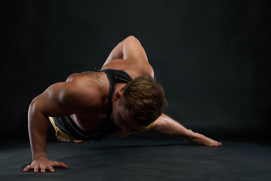 Studio shot of Caucasian male athlete with beautiful muscular body doing one-handed push-ups exercise on floor. Sportsman working out in gym. Sports, fitness and active healthy lifestyle concept