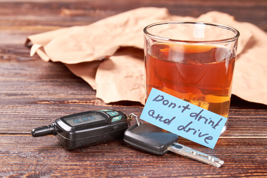Driver keys, glass of alcohol, message. Full glass of alcohol, automobile keys, message, wooden background. Drunk drivers as a social problem.